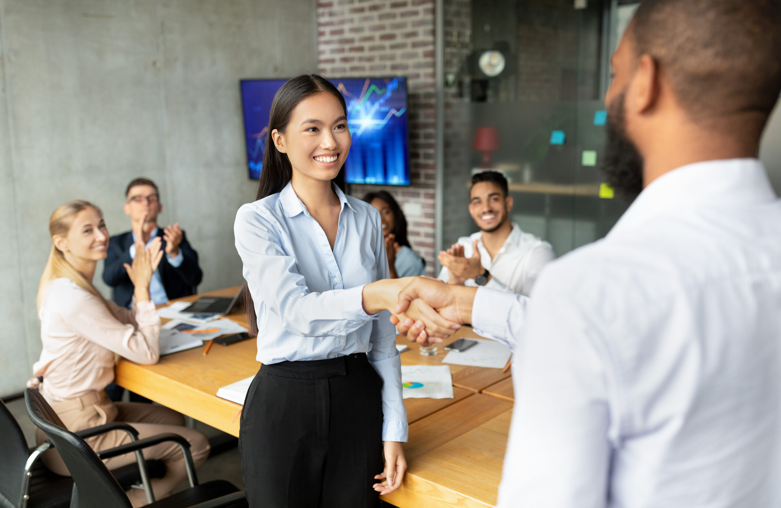 A young professional celebrates a milestone during a sales internship, shaking hands as teammates applaud in the background.