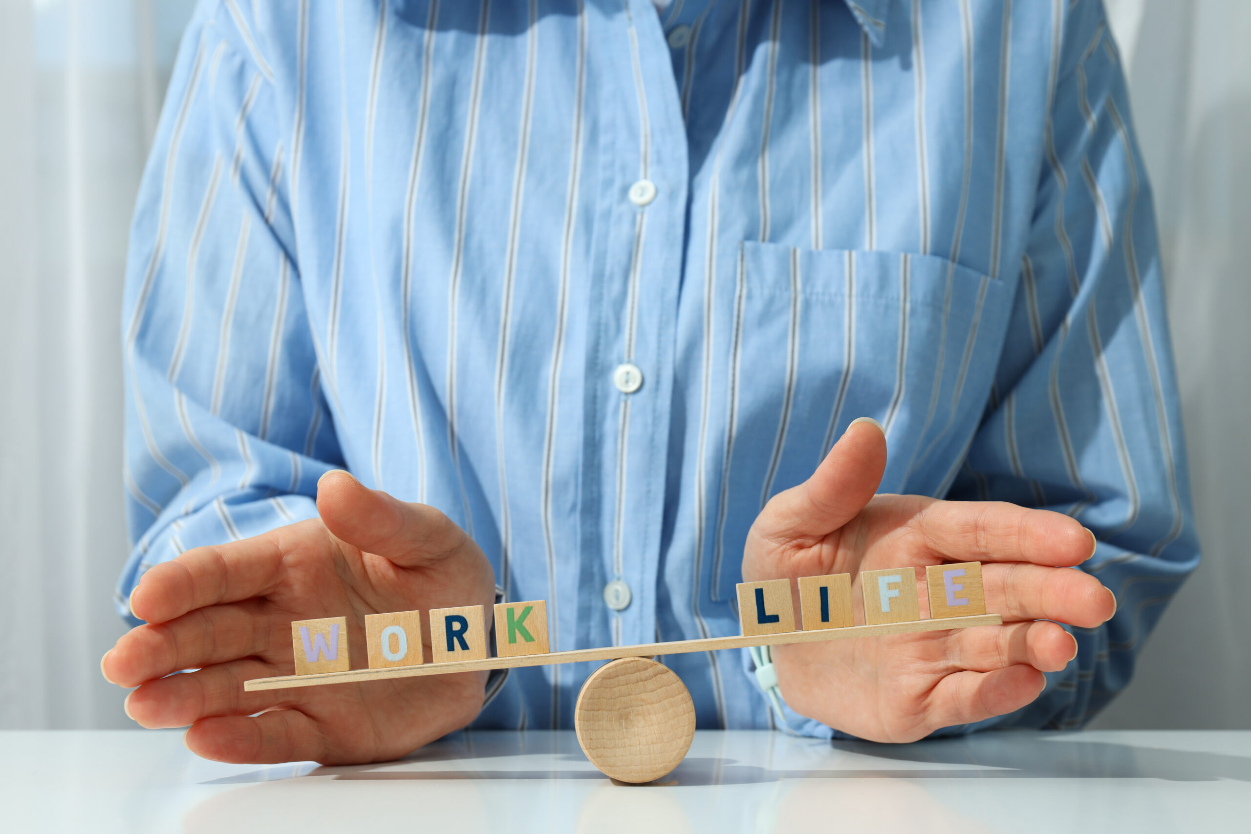Hands balancing “work” and “life” blocks, symbolizing realistic work-life balance tips for a healthier lifestyle.