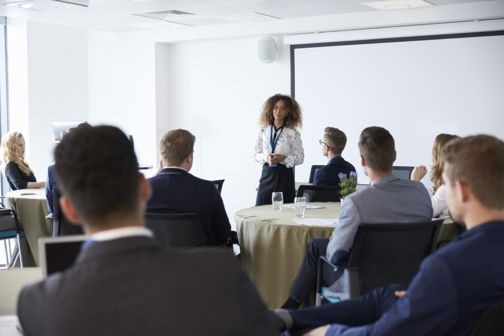 A speaker presenting to a group, highlighting real-world management training and leadership development.